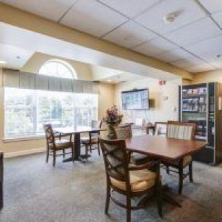A cozy dining area with tables and chairs, featuring large windows and a vending machine.