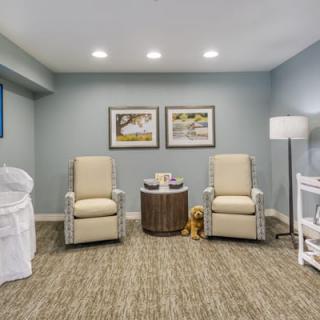 A cozy living room featuring two comfortable chairs, a small round table, artwork on the walls, and a standing lamp in a carpeted area.
