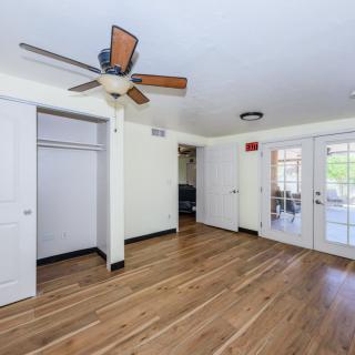 An empty room with hardwood floors, a ceiling fan, and double doors leading outside.