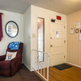 A cozy living room with a recliner chair, mirror on the wall, and a safety gate near the entryway.
