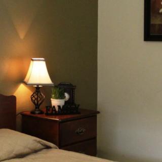 A cozy bedroom with a bed, nightstand, and lamp casting a warm glow.