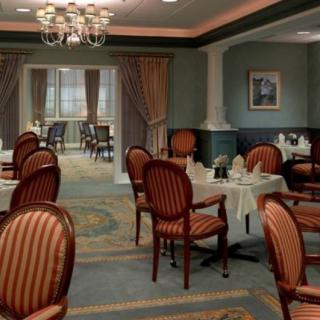 An elegant dining room with neatly arranged tables and chairs, featuring a chandelier and decorative curtains.