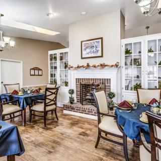 A cozy dining room with elegantly set tables, chairs, and a fireplace adorned with seasonal decorations.