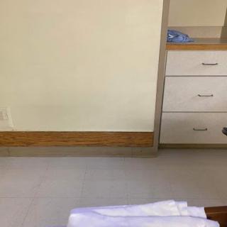 A simple room featuring a dresser, a clean floor, and neatly arranged blankets.