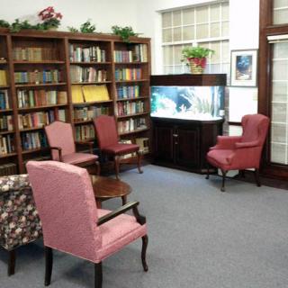 A cozy library corner with bookshelves, armchairs, and an aquarium.