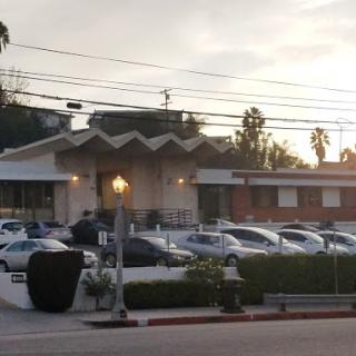A picturesque evening view of a modern architectural building with parked cars, set against a sunset backdrop.