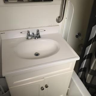 A bathroom sink with a white cabinet and chrome faucet, accompanied by a handrail.