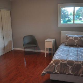 A minimalist bedroom with a single bed, chair, and nightstand on a hardwood floor.