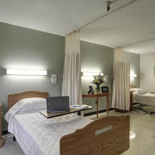 A hospital room with two beds separated by curtains and a laptop on one of the tables.