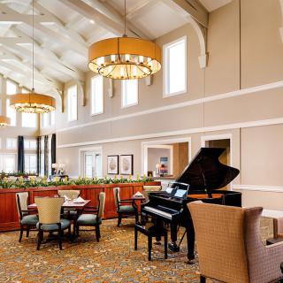 A stylish lounge area featuring a grand piano, elegant chandeliers, and comfortable seating.