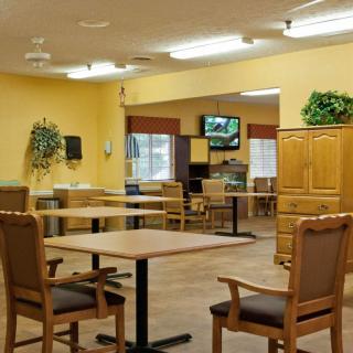 An empty dining area with wooden tables and chairs, decorated with plants and a television mounted on the wall.