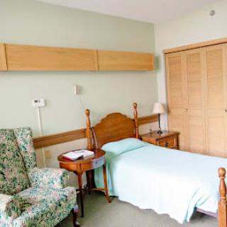 A simple bedroom with a single bed, an armchair, and wooden furniture.