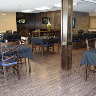 A spacious and modern restaurant interior featuring wooden flooring, dark tables, and a welcoming bar area.
