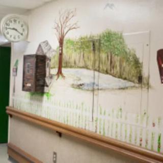 A hospital hallway features a mural depicting a serene nature scene with a tree and pond, accompanied by a clock on the wall.