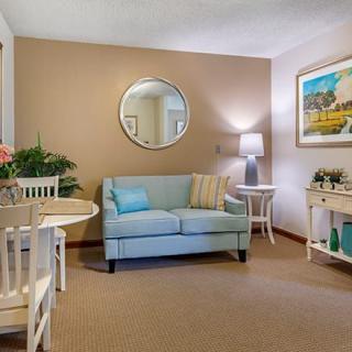 A cozy living room with light blue sofa, round mirror, side tables with lamps, and decorative artwork.