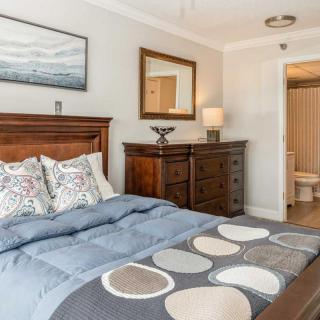A cozy bedroom with a neatly made bed, wooden dresser, mirror, and decorative lamp.