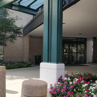 A welcoming entrance featuring a glass canopy and colorful flower beds.