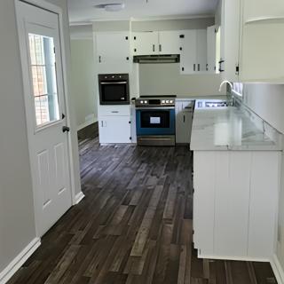 A modern kitchen with white cabinets and dark wood flooring.