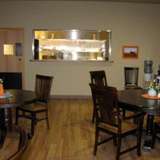 A cozy restaurant dining area with wooden tables and chairs facing a visible kitchen.
