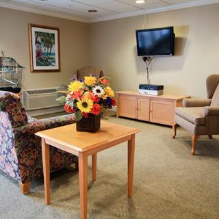 A cozy living room with comfortable seating, a bouquet of flowers on the table, and a television mounted on the wall.