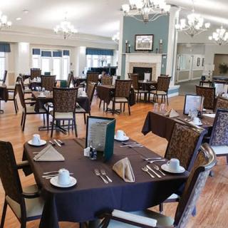 An elegant dining room with neatly arranged tables and chairs, featuring chandeliers and a fireplace.