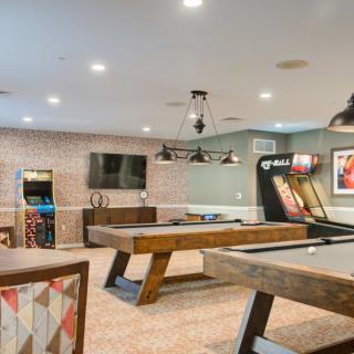 A modern game room featuring pool tables, an arcade machine, and a wall-mounted TV.