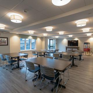 A modern, spacious dining area with multiple tables and chairs, illuminated by ceiling lights.
