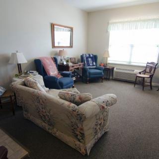A cozy living room with a sofa, armchairs, a large window, and decorative elements.