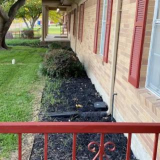 A landscaped garden bed along the side of a house with mulch and bushes.