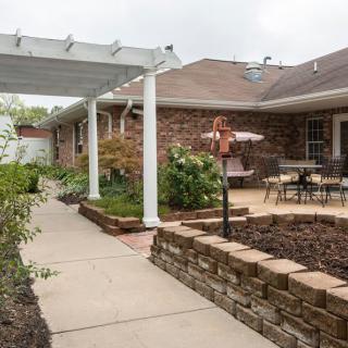 A cozy backyard patio with a pergola and garden, featuring outdoor seating and a walkway.