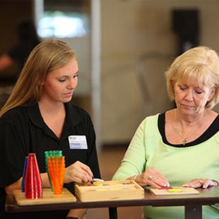 A young woman assists a senior woman with an engaging activity, promoting connection and learning.