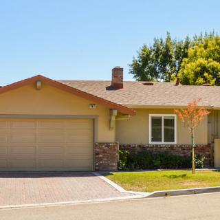 A single-story suburban house with a driveway and garage, surrounded by trees.
