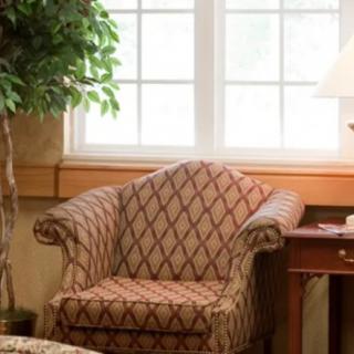 A cozy living room corner featuring an armchair, side table with a lamp, and a decorative plant by the window.