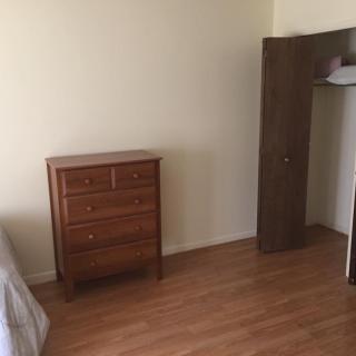 A minimalist bedroom with a wooden dresser and an open closet.