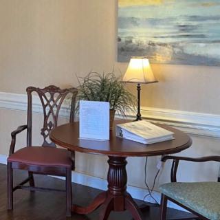 A cozy corner with a round wooden table, two chairs, a table lamp, and wall art.