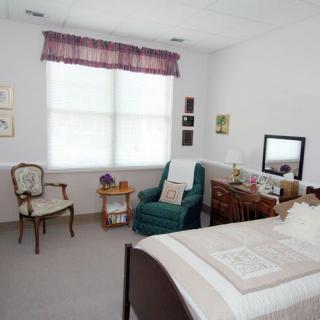 A cozy bedroom with simple decor, featuring a bed, upholstered chair, and wooden furniture.