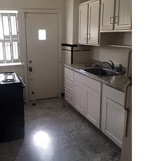 A compact apartment kitchen with white cabinets and a stainless steel sink.