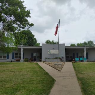 A view of a building with an American flag in front, surrounded by grass and under a cloudy sky.