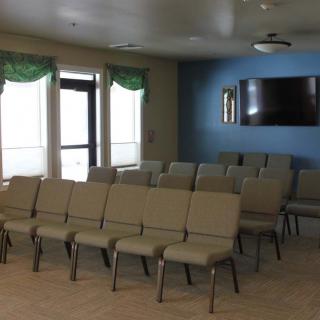 An empty meeting room with rows of chairs facing a large television on a blue wall.