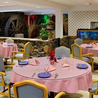 A cozy restaurant dining area with round tables set for meals, featuring a decorative water wheel in the background.