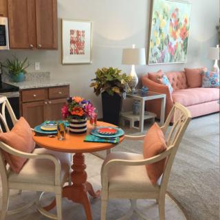 A cozy dining and living space featuring a vibrant dining table set with colorful plates and an inviting living area with floral artwork and plants.