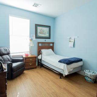 A neatly arranged bedroom with blue walls, featuring a single bed, armchair, nightstand, and wall art.