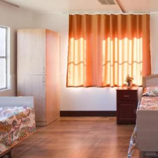 A tidy bedroom with two single beds, orange curtains, and wooden furniture.
