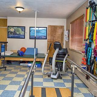 A rehabilitation room equipped with exercise equipment, therapy bands, parallel bars, and a treatment table.