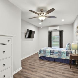 A modern bedroom featuring a mounted TV, ceiling fan, and a neatly made bed with a patchwork quilt.