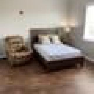 A cozy bedroom with a bed and armchair on a wooden floor.