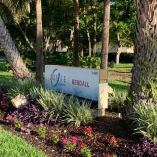 A sign surrounded by vibrant flowers and lush trees in a park setting.