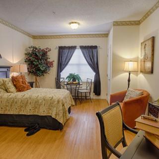 A cozy bedroom interior with stylish decor featuring a comfortable bed, seating area, and natural lighting from a window.