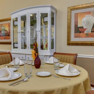 An elegantly set dining table with a china cabinet and artwork in the background.