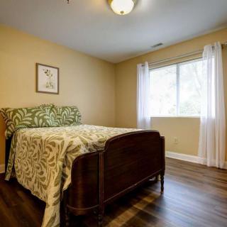 A cozy bedroom with a wooden bed and patterned bedding set, featuring a large window with white curtains.
